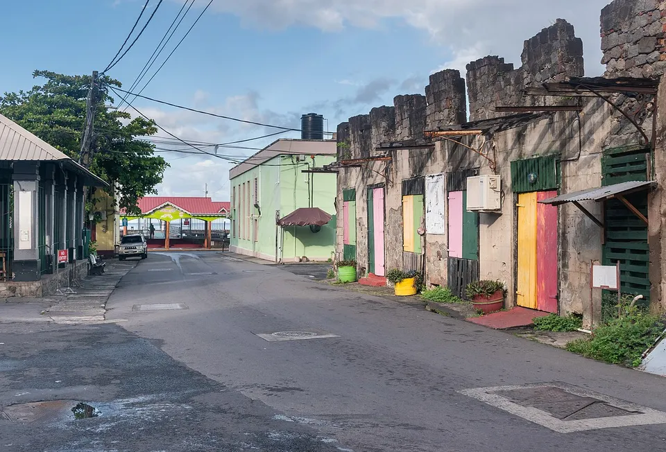 King George V Street à Roseau : une rue vide, des façades de pierre aux portes jaunes, roses et vertes, et un pavillon au toit rouge au bout de la rue, sous un ciel bleu