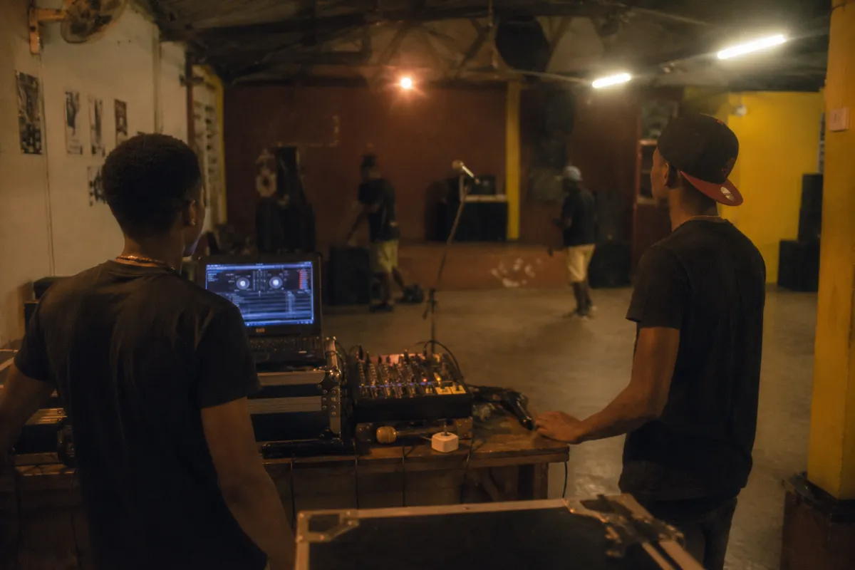 Petite salle de showcase en Guadeloupe en 2016, table DJ, ordinateur, micro sur pied, enceintes en installation, ambiance de soirée locale avant l'arrivée du public