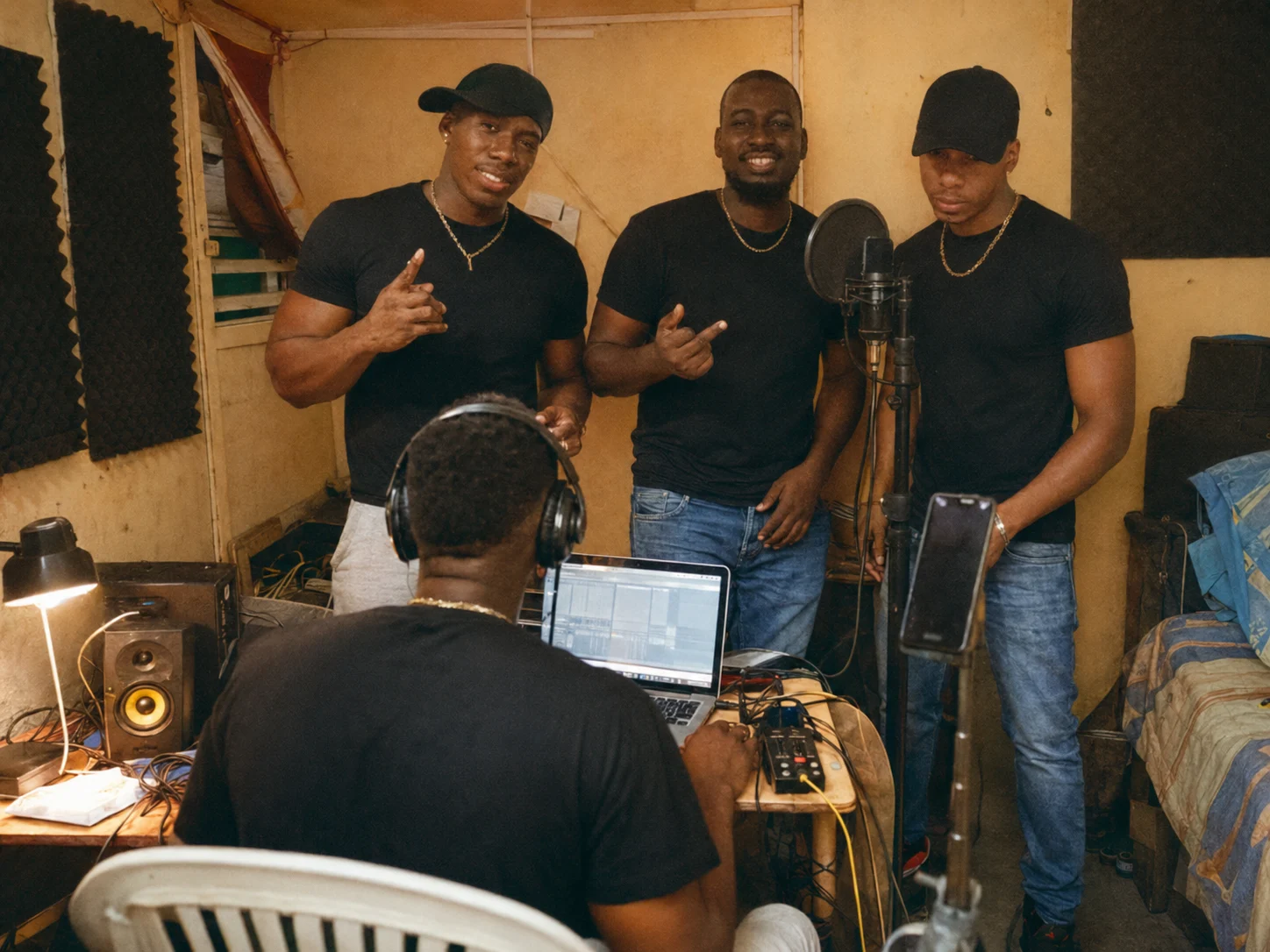 Team Bwè Tou Sa dans un studio maison guadeloupéen en 2020 avec Gama Lab vu de dos au laptop, micro, casque, câbles, enceintes et lumière chaude