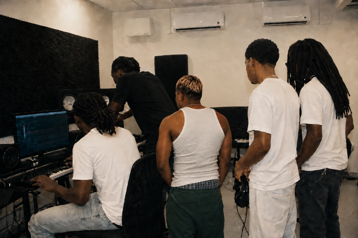Young Guadeloupean artists and producers seen from behind in the MJC des Abymes studio around a computer and studio monitors