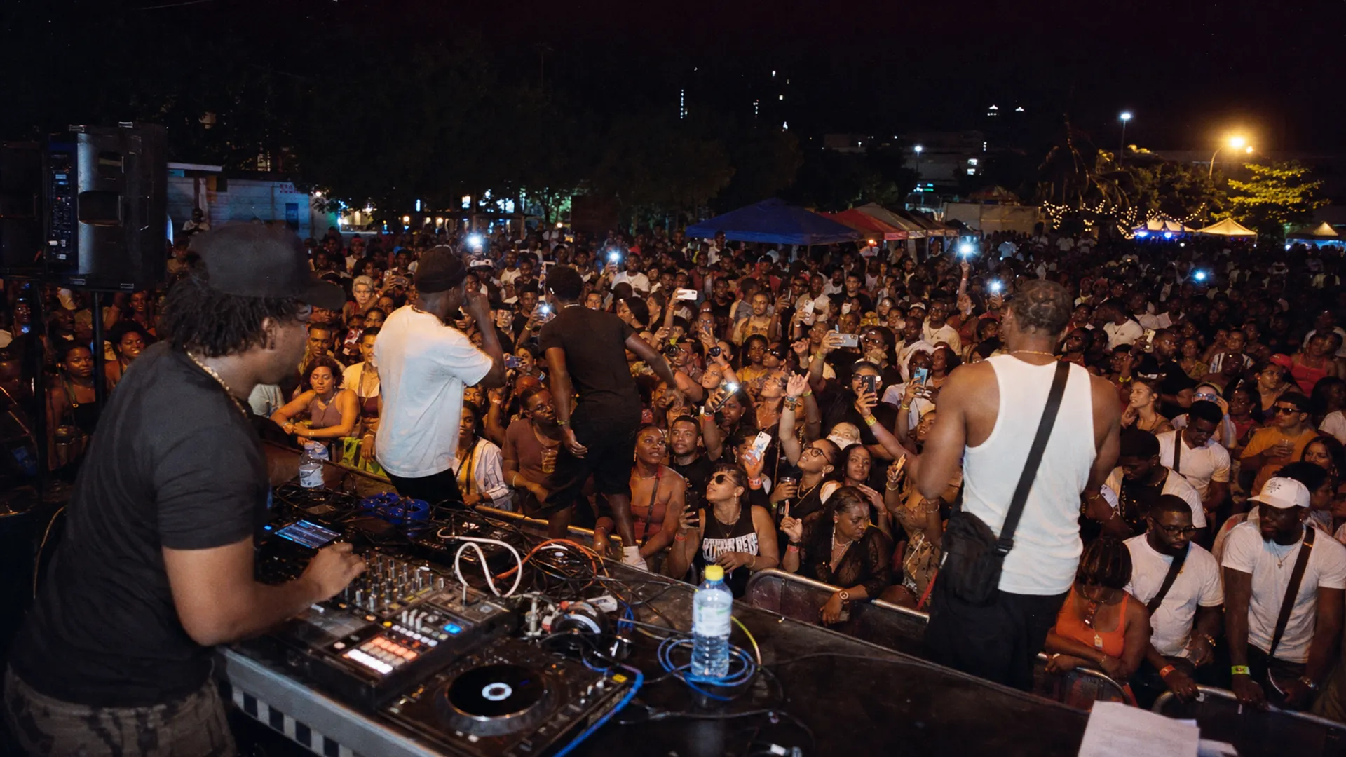 Nighttime Caribbean festival scene with DJ, crowd, phones and lights, evoking Bouyon's global circulation