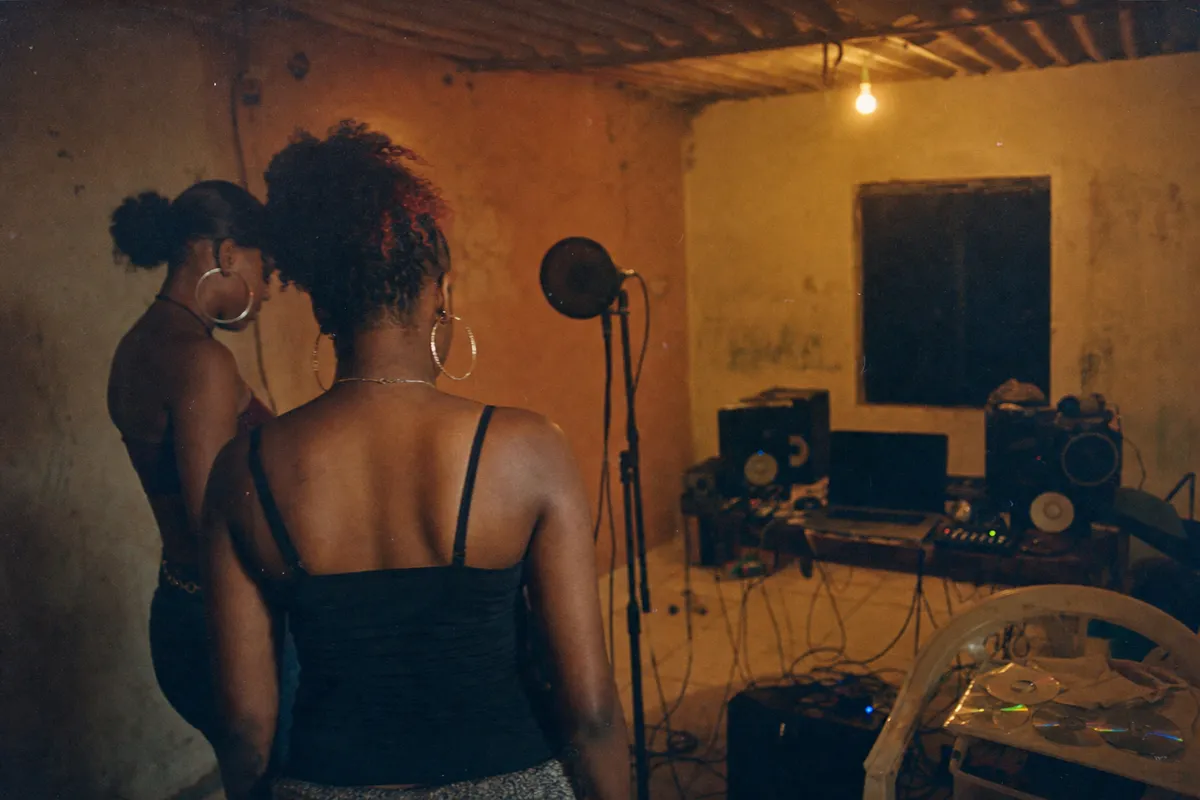Underground Bouyon rehearsal room in Guadeloupe in the early 2010s, female silhouettes near a microphone and small sound system
